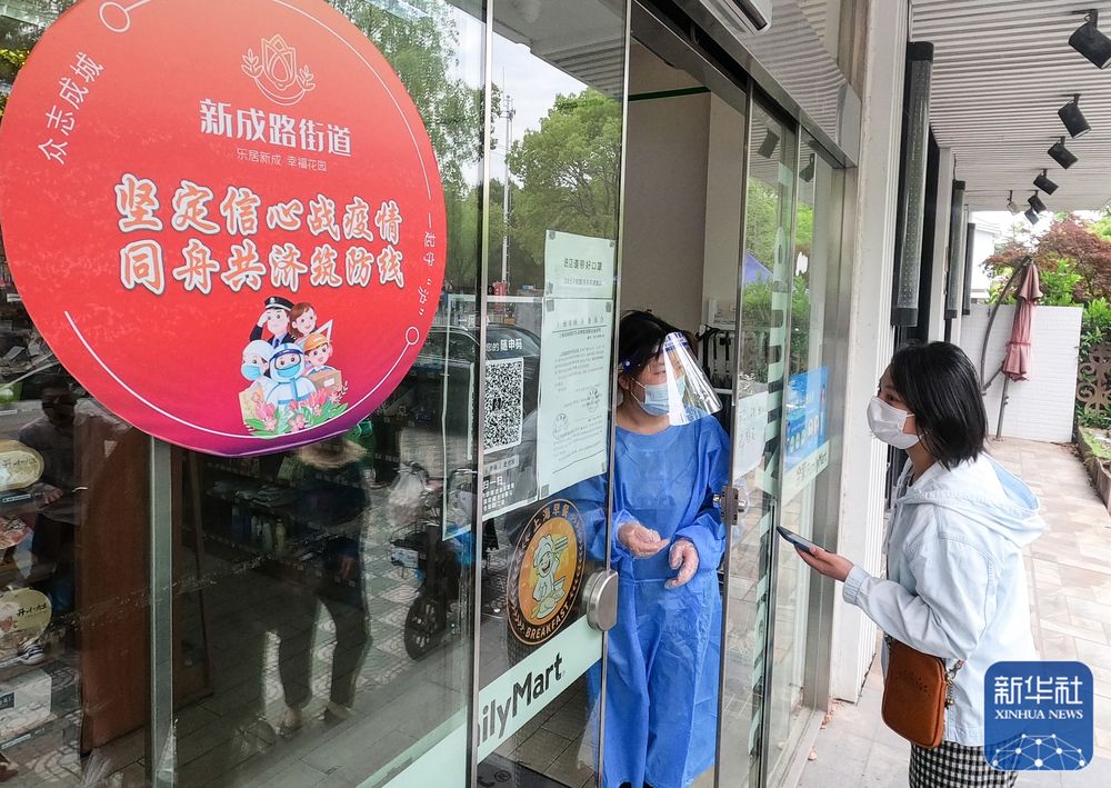 上海市嘉定區新成路街道（エリア）でQRコードをスキャンしてコンビニに入店する人（寫真右）。同エリアではコロナ感染対策基準を満たすと認定された商店などに赤い円形のシールを掲示している（5月9日撮影）。