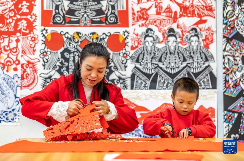 黔西市文化館のアトリエで、新年を迎える伝統工蕓の「切り紙」作りを學生に教える、黔西切り紙無形文化遺産伝承人の岳紅霞さん（寫真左、12月26日撮影?範暉）。